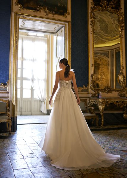 Hellenic style wedding dress model with thin spaghetti straps, decorated with 3D flowers, and skirts made of organza fabric